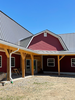 A red barn with a metal roof, white seamless rain gutters, and a wooden porch.