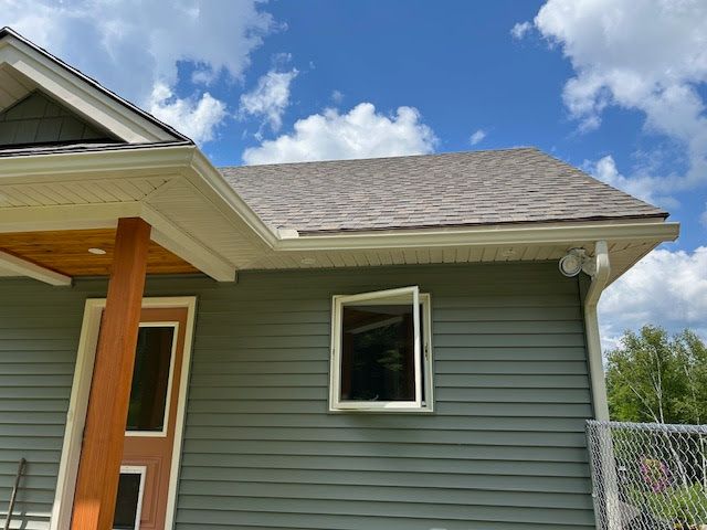 A house with white rain gutters and a window on the side of it.