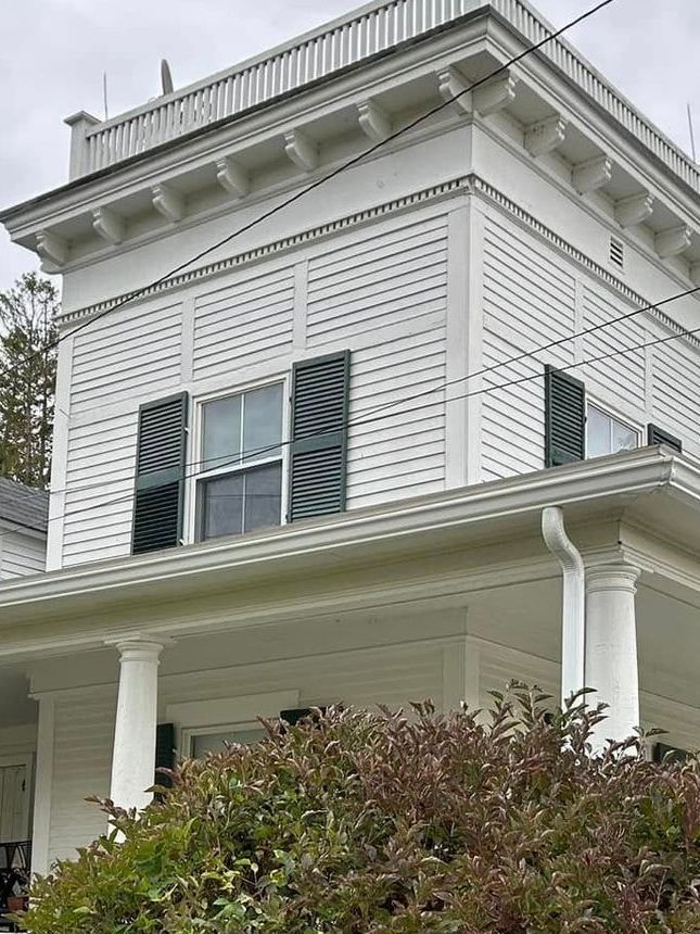 A white house with white seamless rain gutters, also with black shutters on the windows and a porch.