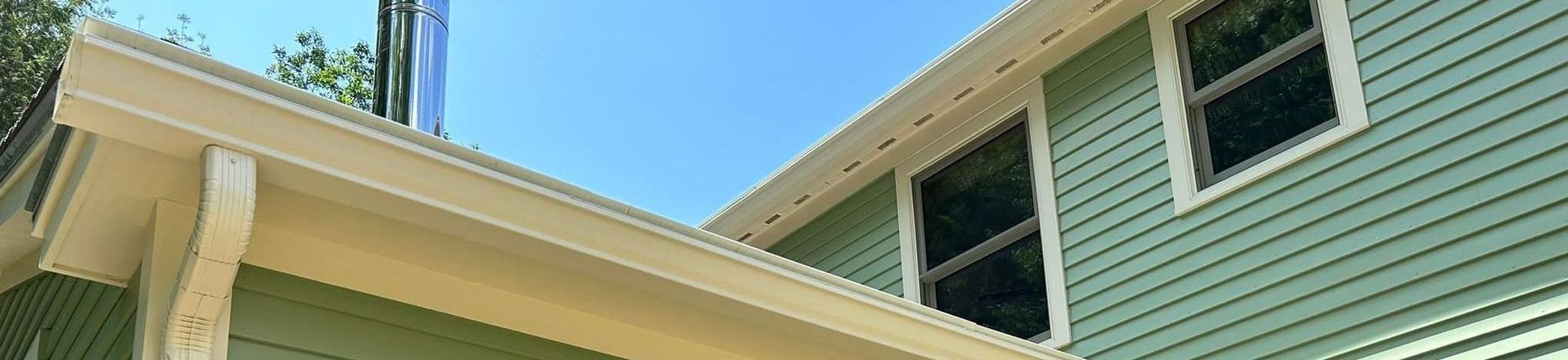 A green house with yellow seamless rain gutters and a porch and a blue sky in the background.