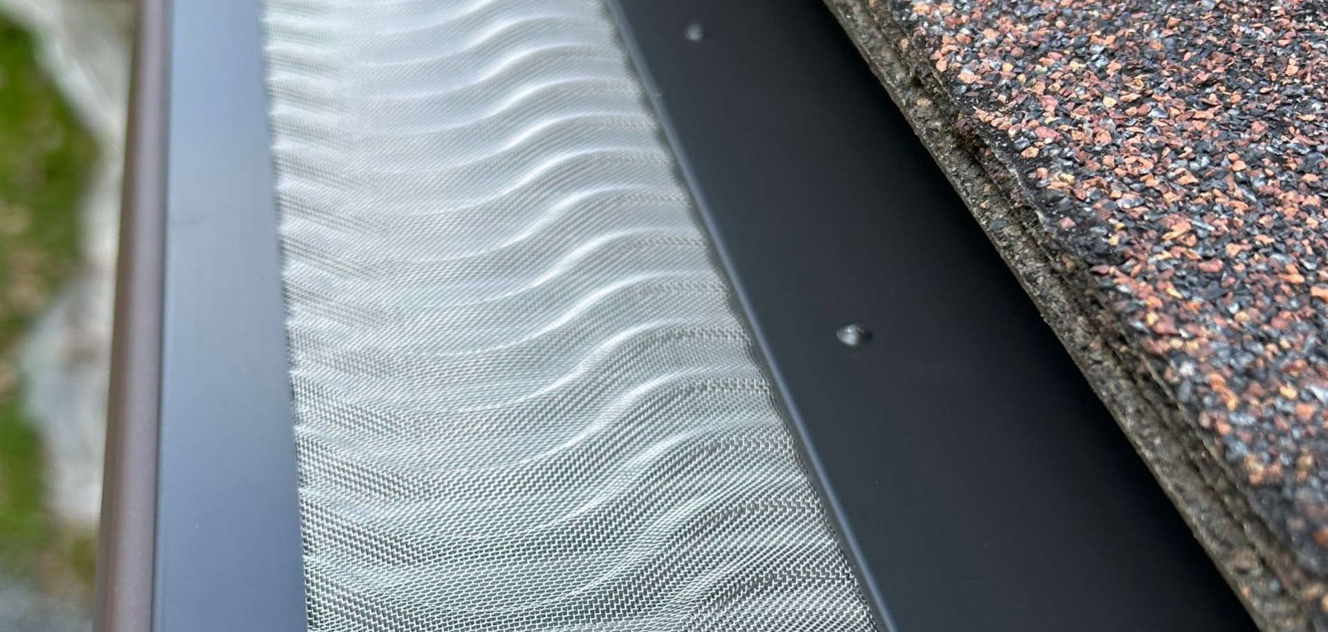 Close-up of a gutter guard in Northern Vermont over a rain gutter, with gravel roofing along the edge