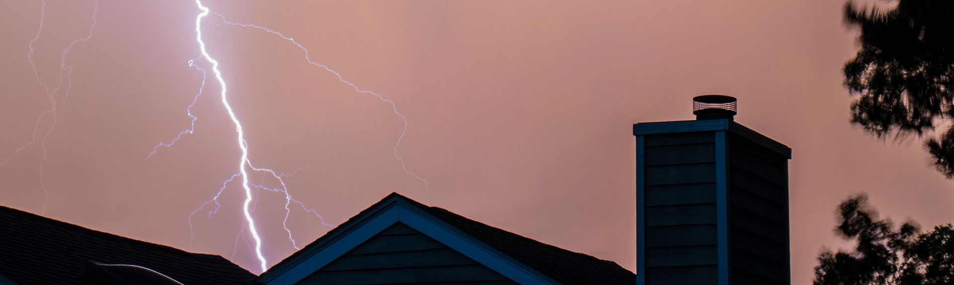 Lightning strikes over rooftops at dusk, with a pink-purple storm sky.