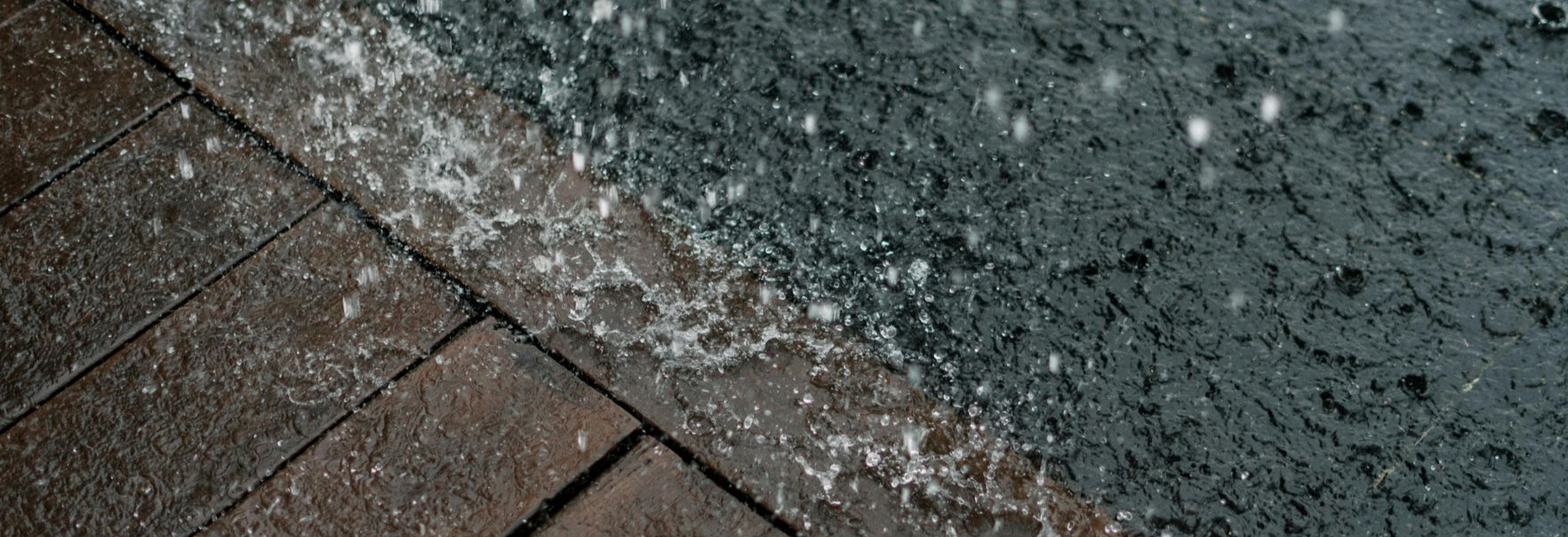 Heavy summer rain splashing and pooling, illustrating the potential for water damage and rot without proper downspout