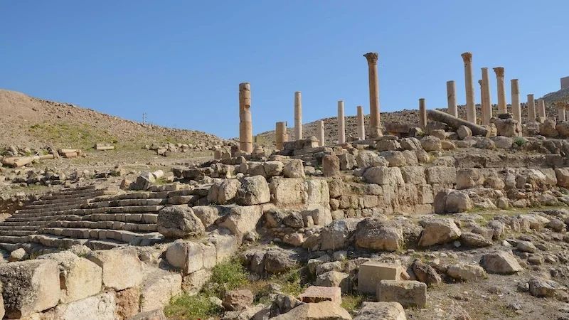 Ancient stone ruins with columns on a rocky hillside under a clear sky