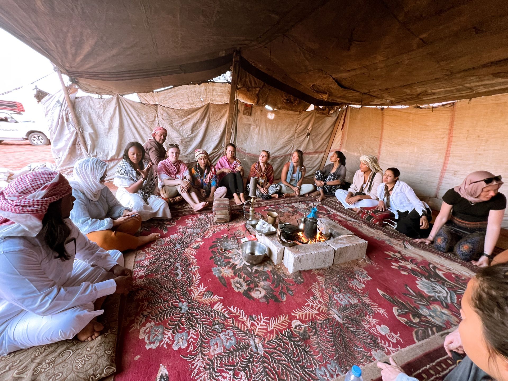 Group of travelers sitting on rugs inside a large Bedouin tent in the Jordanian desert