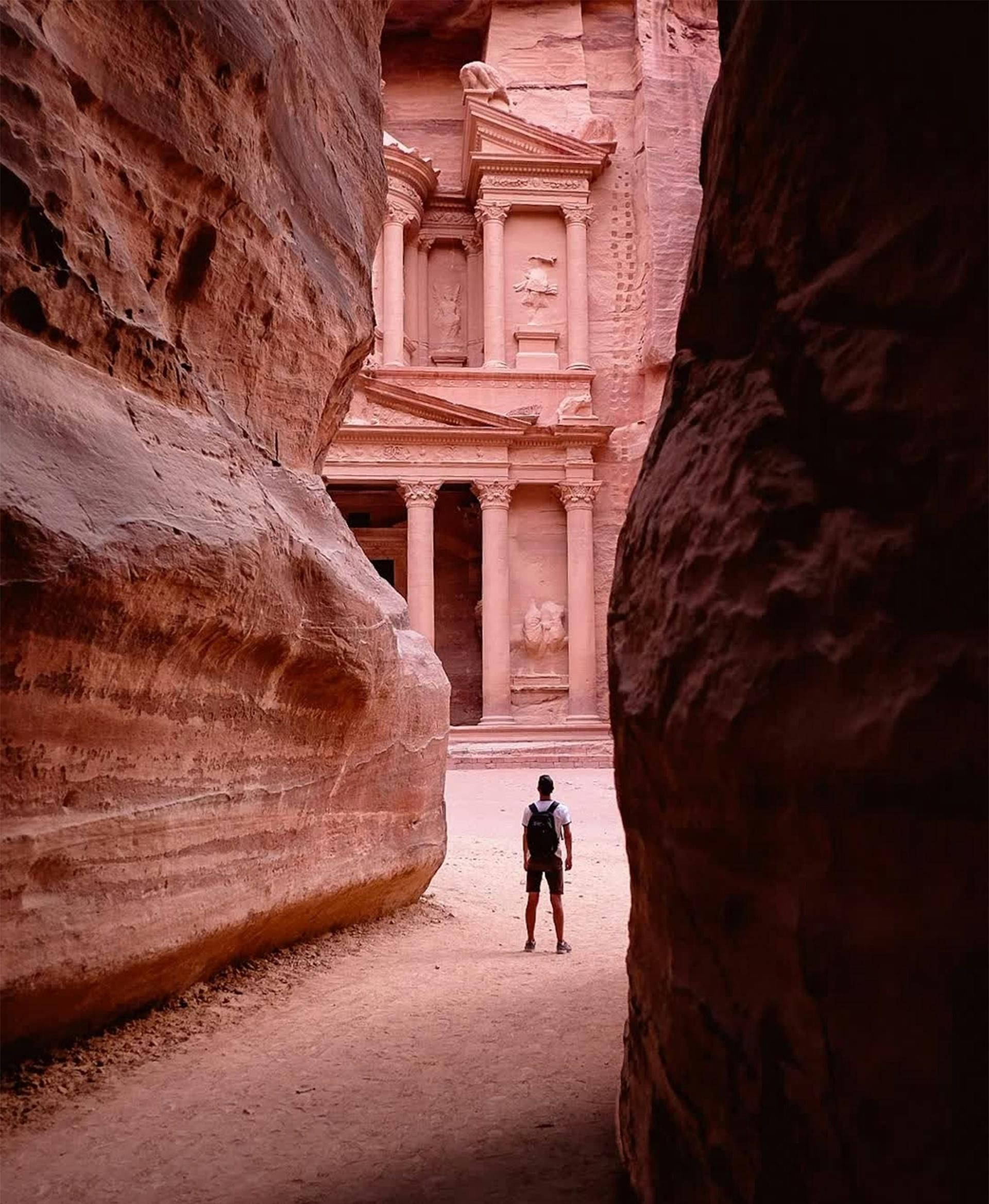 Person standing in a narrow canyon before Petra’s sandstone façade