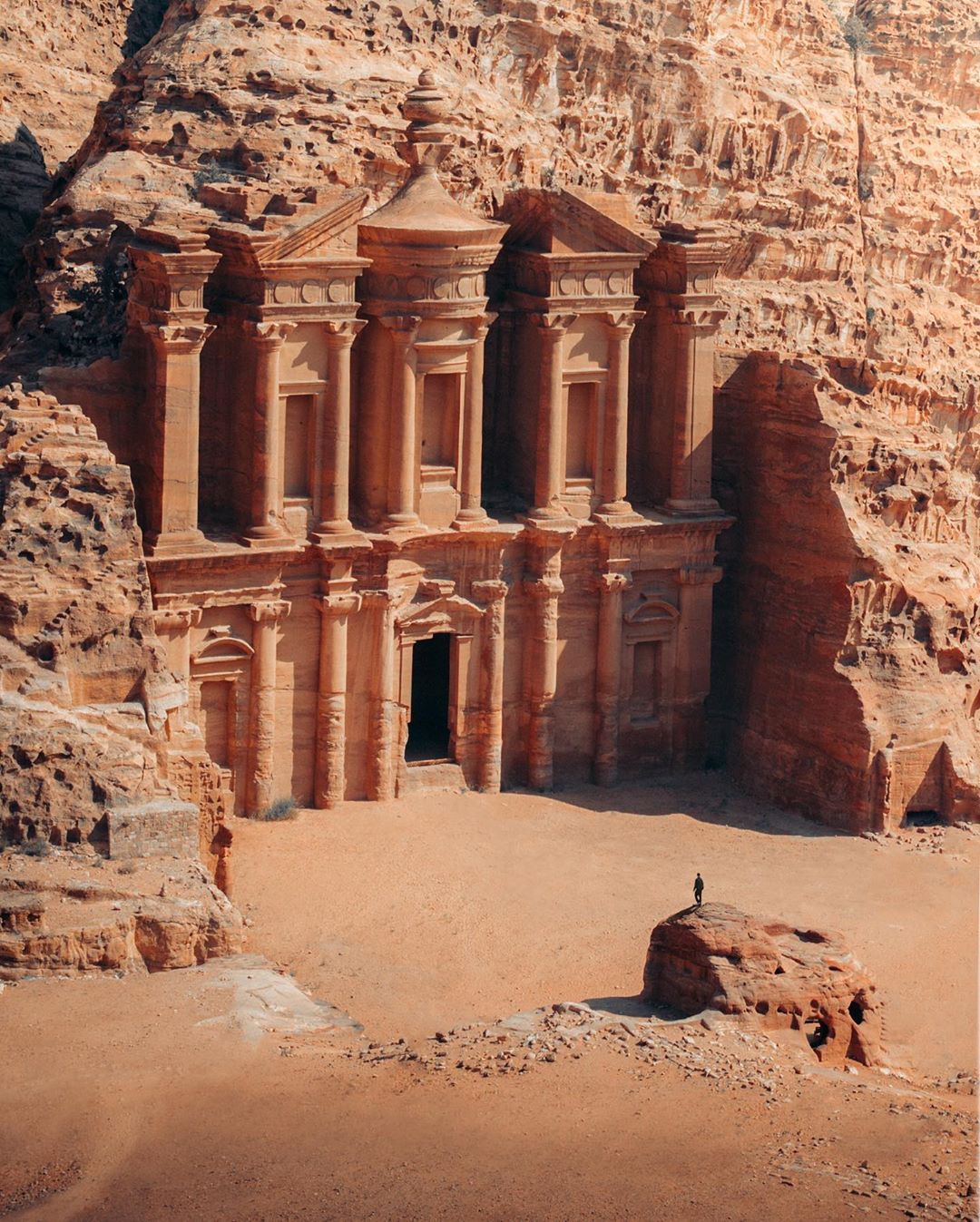 Ancient rock-cut temple facade carved into a sandstone cliff in a desert canyon.