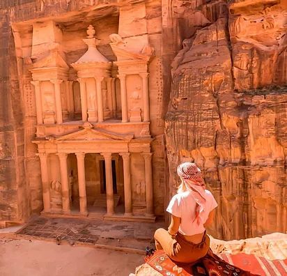 Person overlooking Petra’s Treasury carved into orange sandstone cliffs in desert light