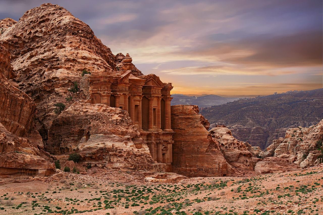 Ancient rock-cut temple carved into a red sandstone cliff at sunset, overlooking a desert valley