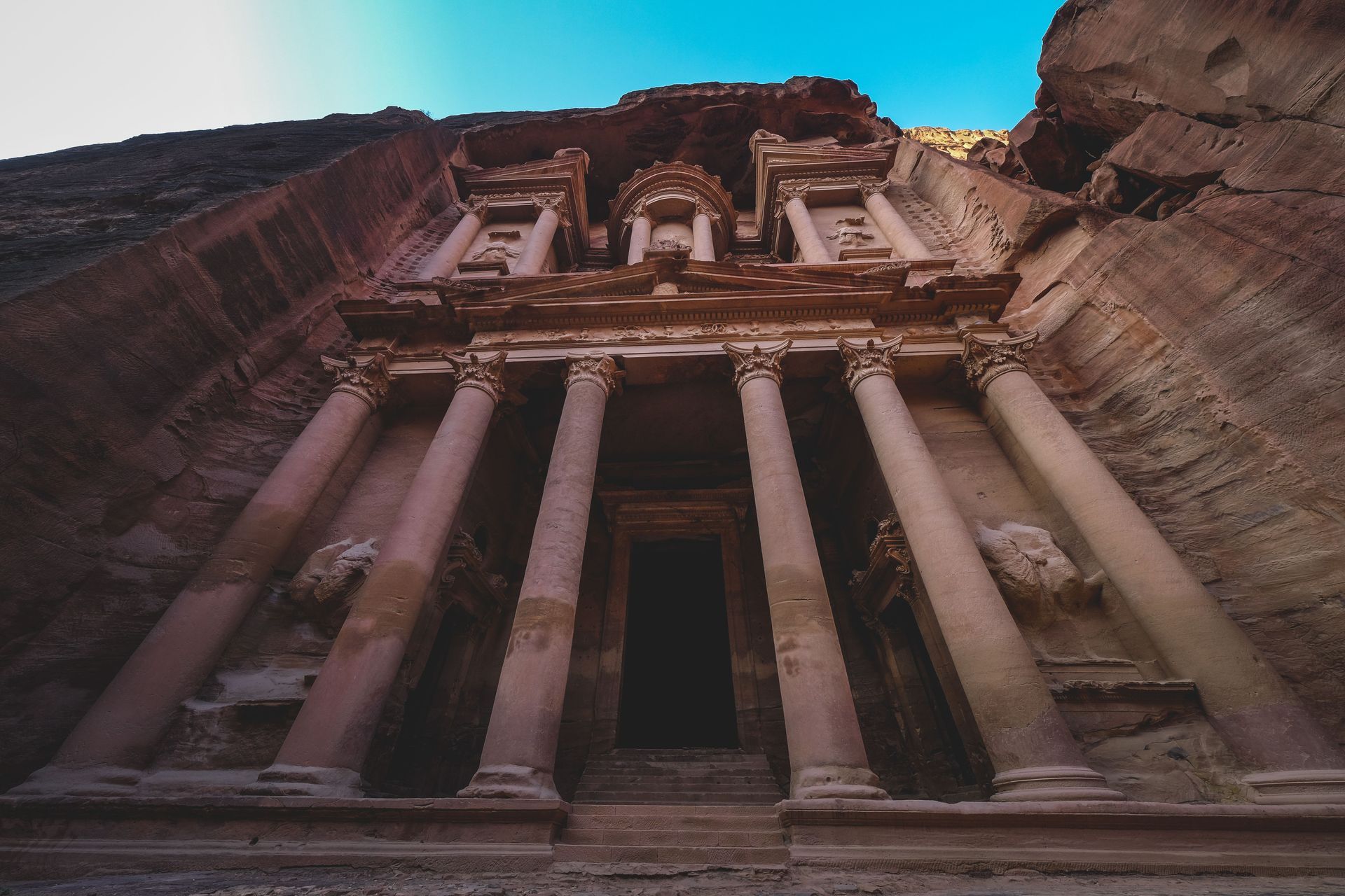 Ancient rock-cut temple facade with tall columns carved into a cliff under a blue sky