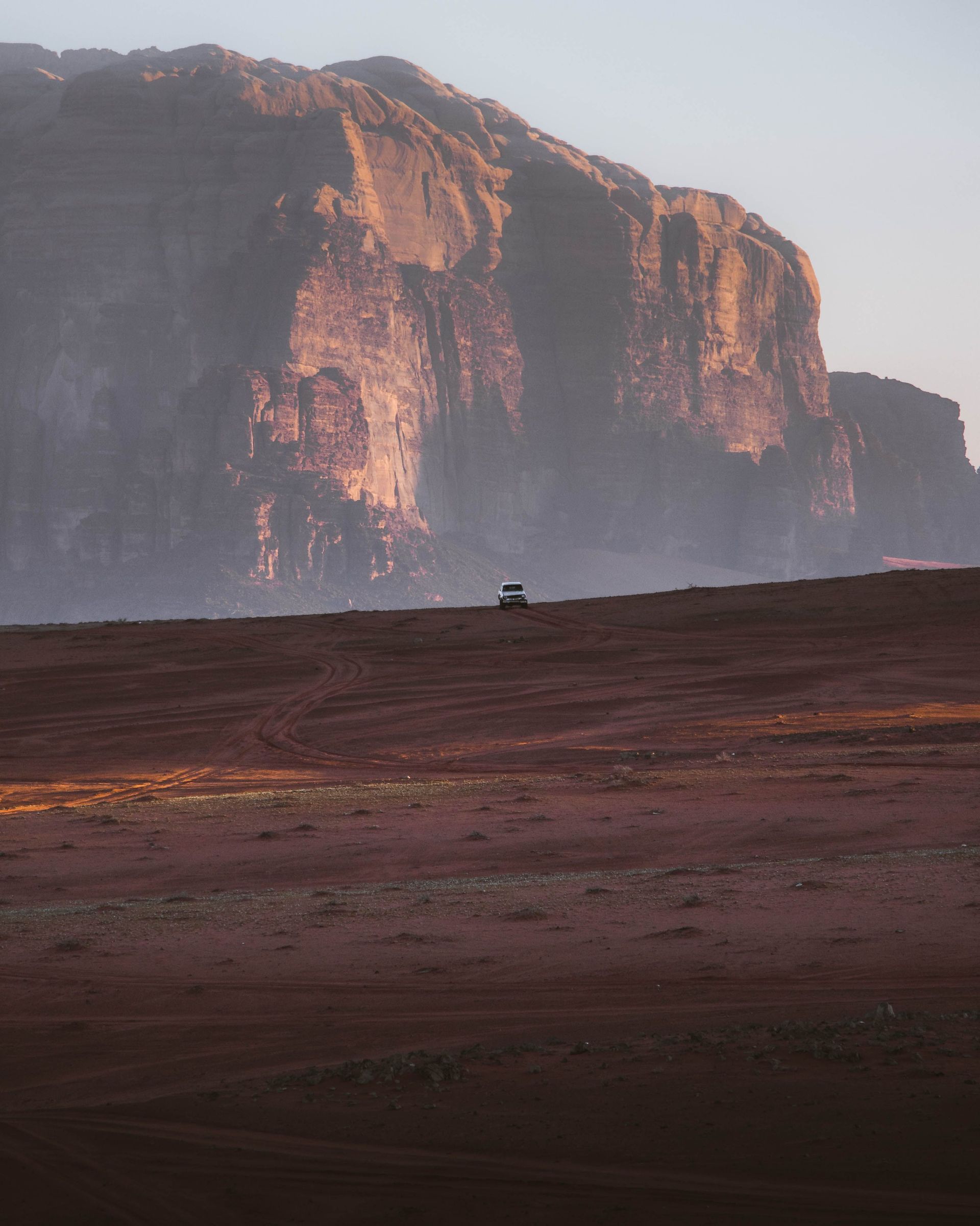 Sunlit cliff above a barren reddish plain at dawn or dusk