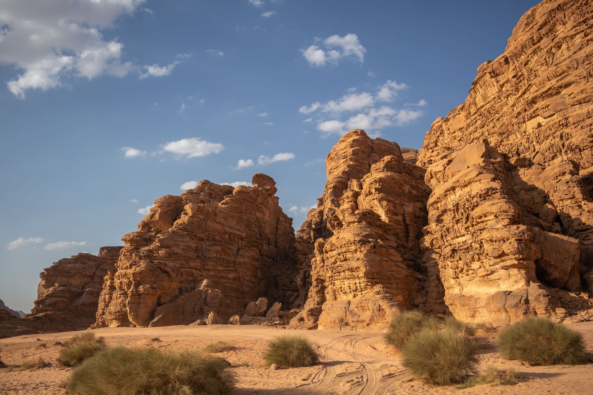 Rocky desert cliffs under a blue sky with scattered clouds and sparse shrubs