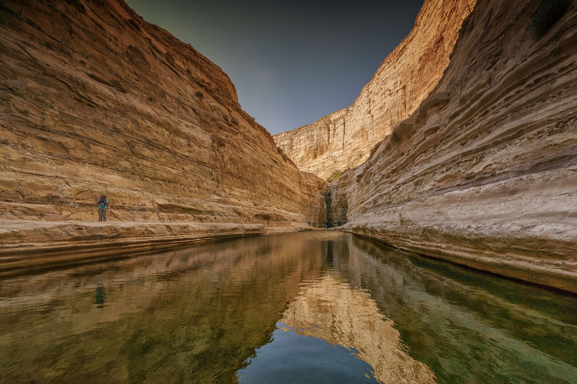 Layered sandstone canyon walls reflected in still water, in the Jordan Rift Valley landscape