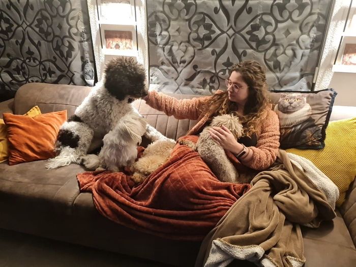 Vrouw zit op een bank en aait een pluizige zwart-witte hond in een gezellige woonkamer.