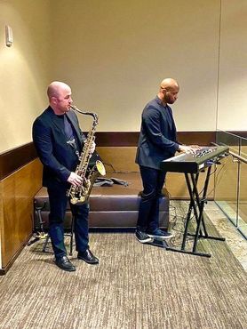 Two men are playing saxophones and keyboards in a room.