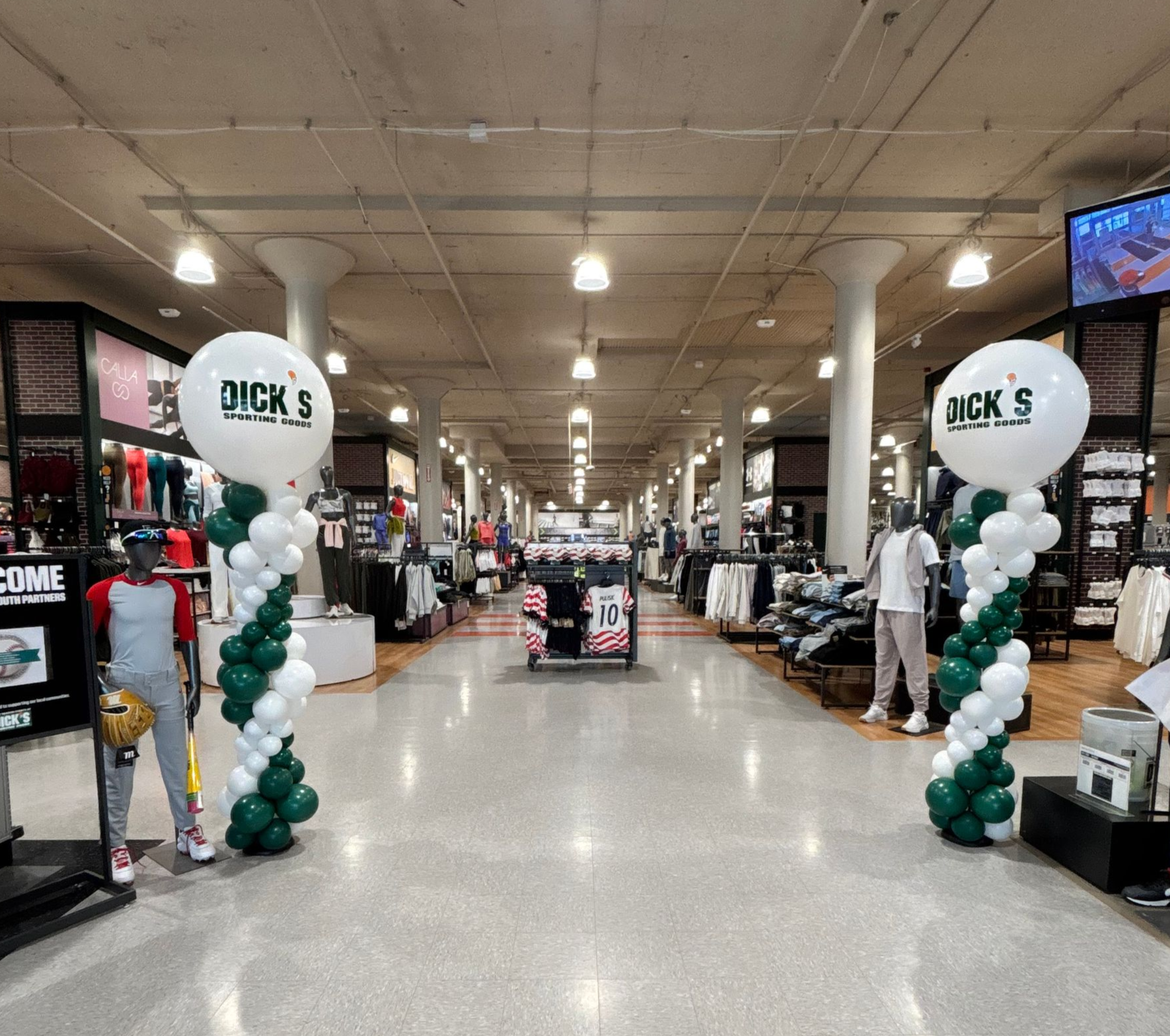 Two green and white organic bubble balloon columns with oversized branded balloons displayed at the entrance inside Dick’s Sporting Goods for an employee appreciation event by Designs by Jo Jo’s Creations in Canton, Ohio.