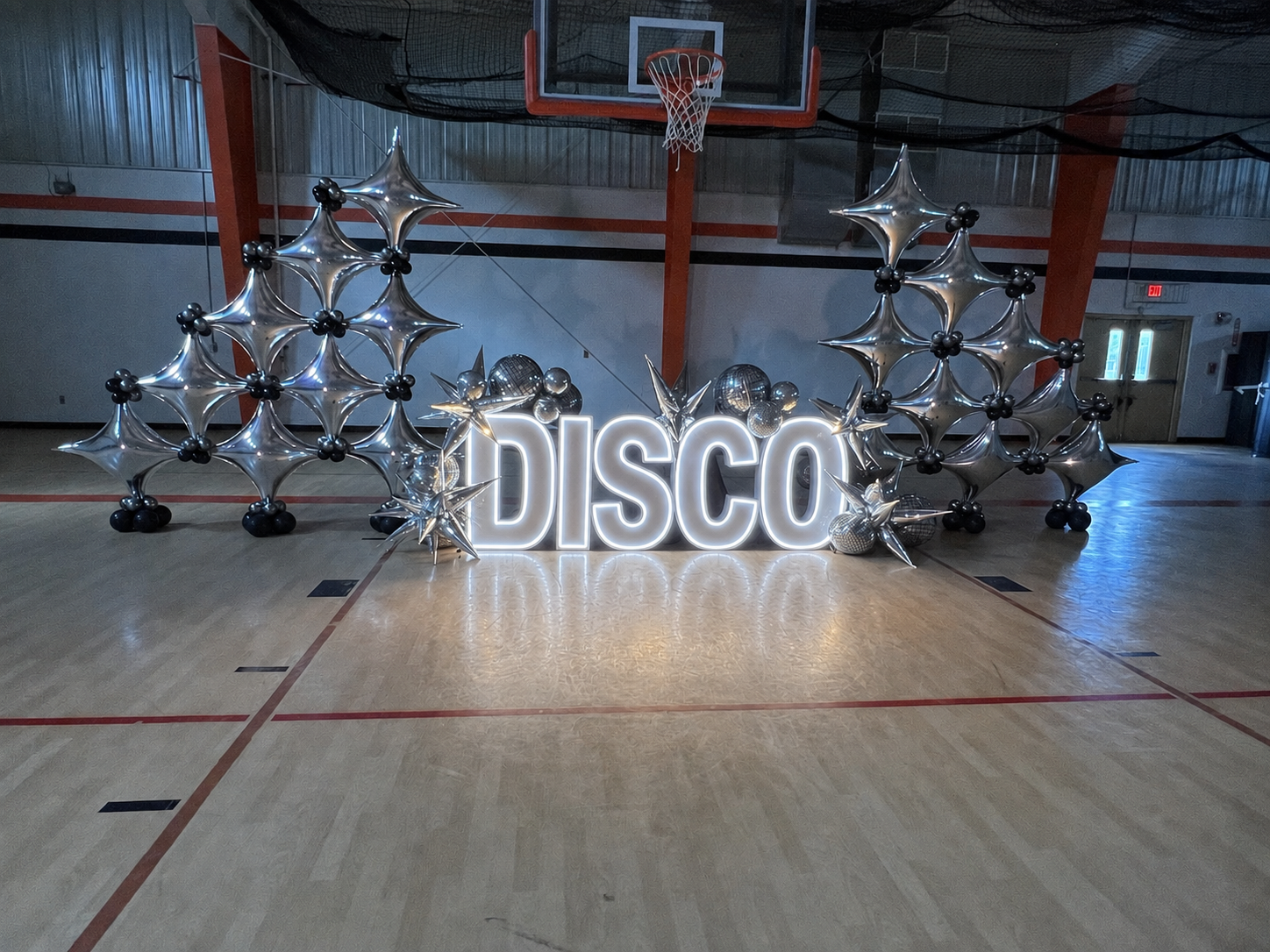 White illuminated “DISCO” LED marquee letters with silver balloon structures, black accents, disco balls, and metallic starbursts.