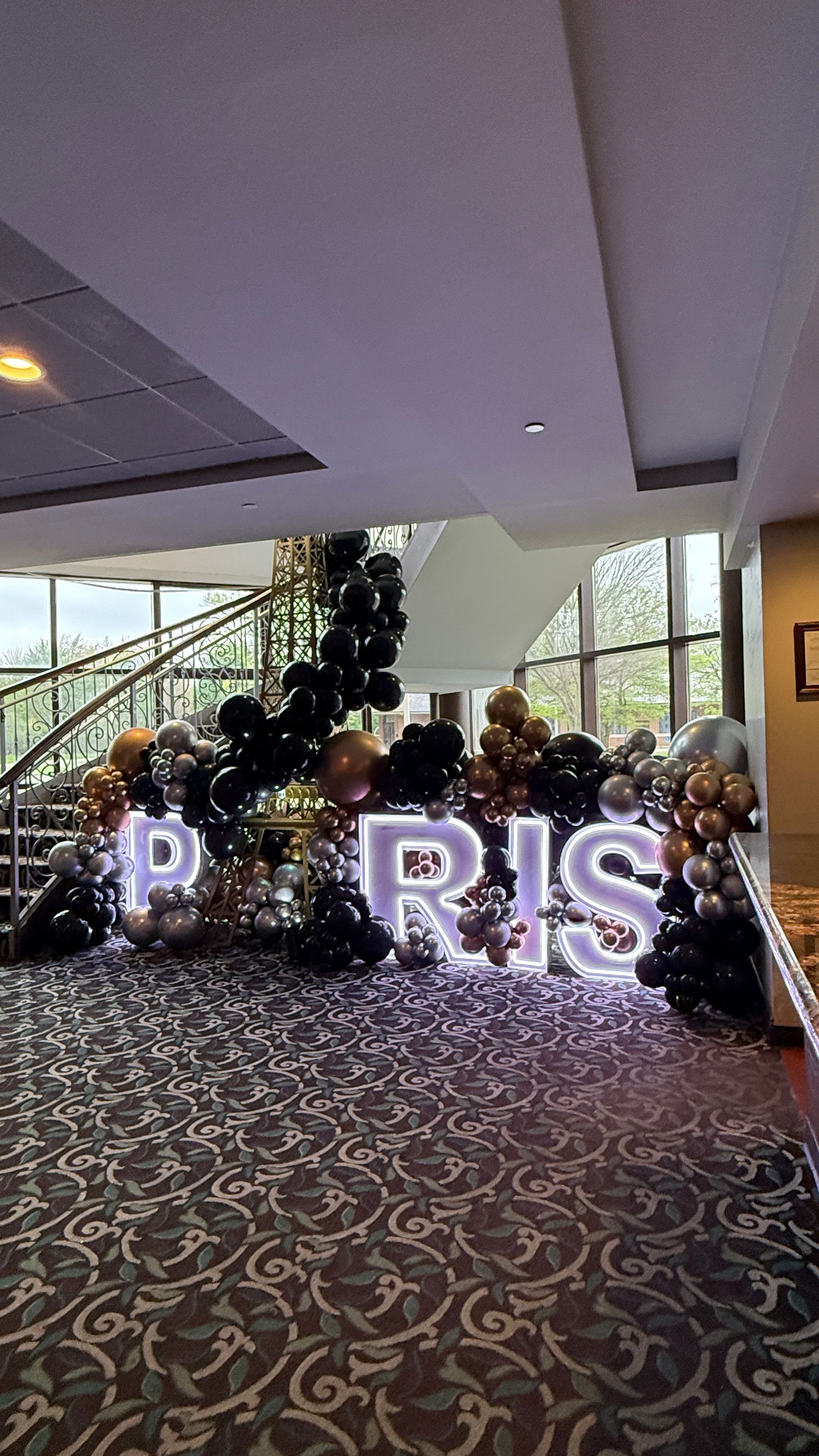 Illuminated PARIS marquee letters with Eiffel Tower props and black, gold, silver, and champagne balloon décor.