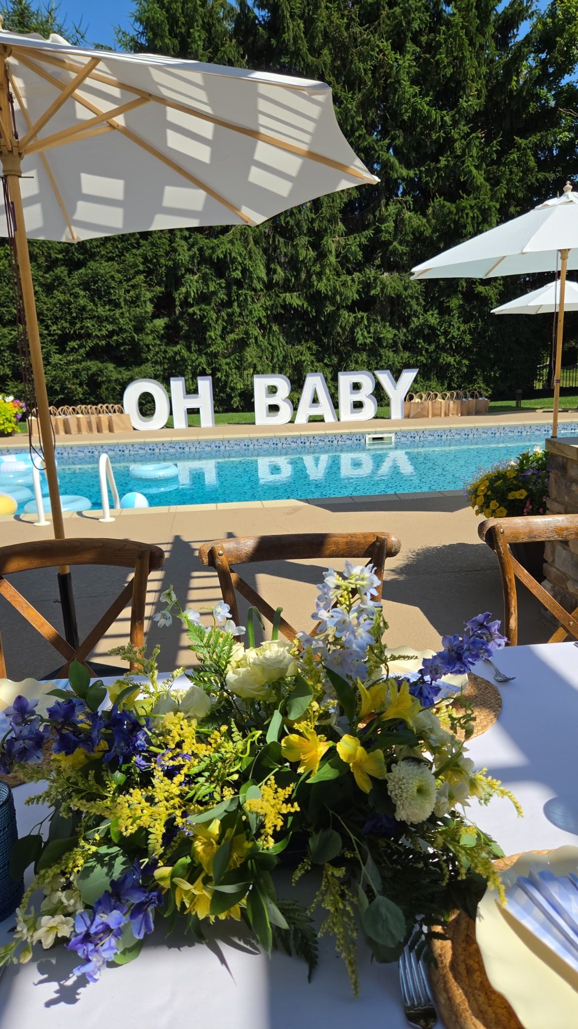Oversized white “OH BABY” marquee letters displayed beside an outdoor swimming pool for a baby celebration.