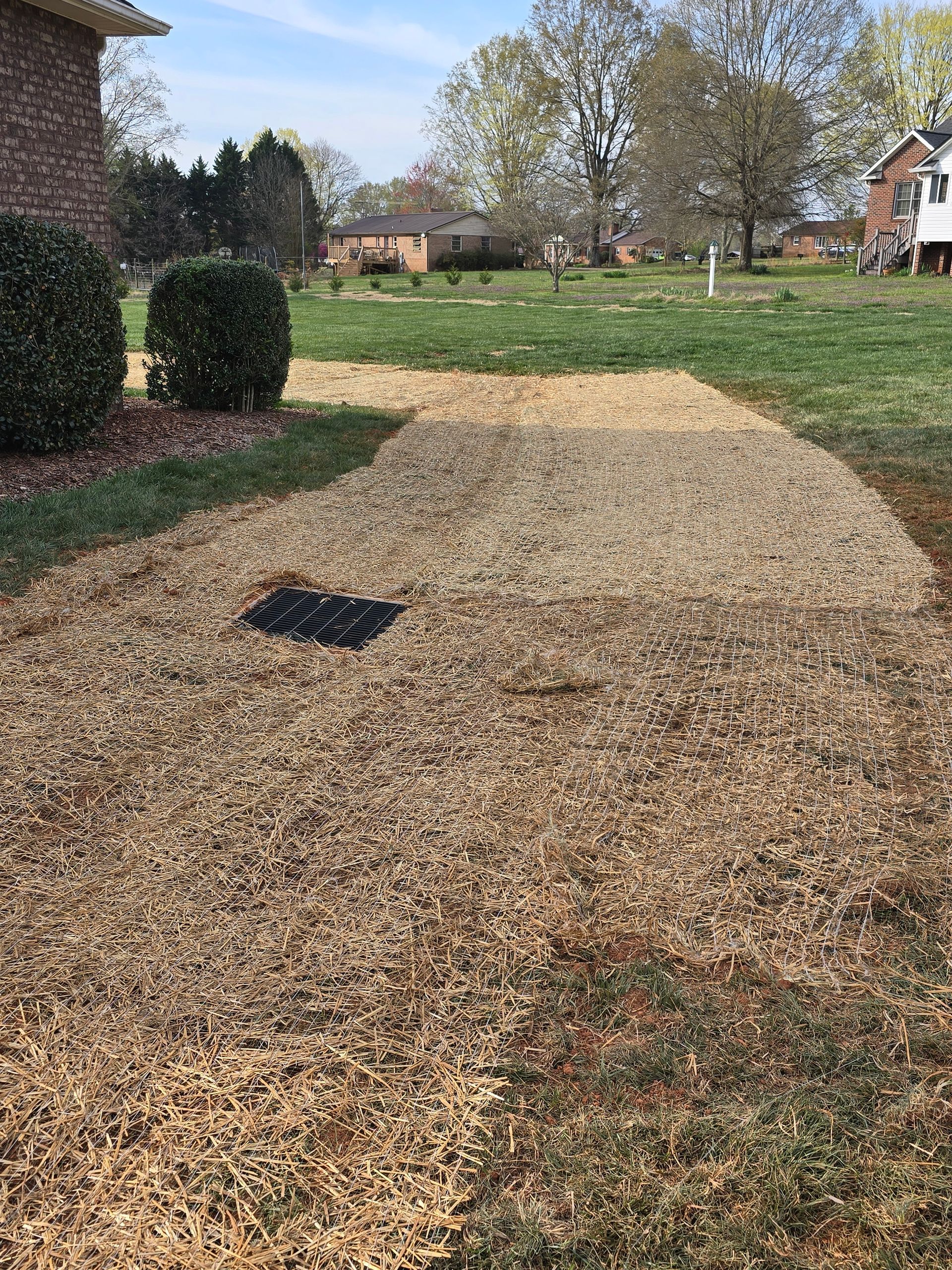 Gravel driveway beside a brick house, with a green lawn and trees in the background.