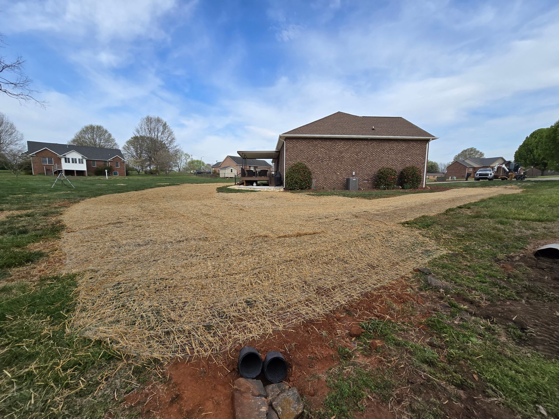 Gravel yard behind a brick house under a blue sky, with a drain pipe in the foreground