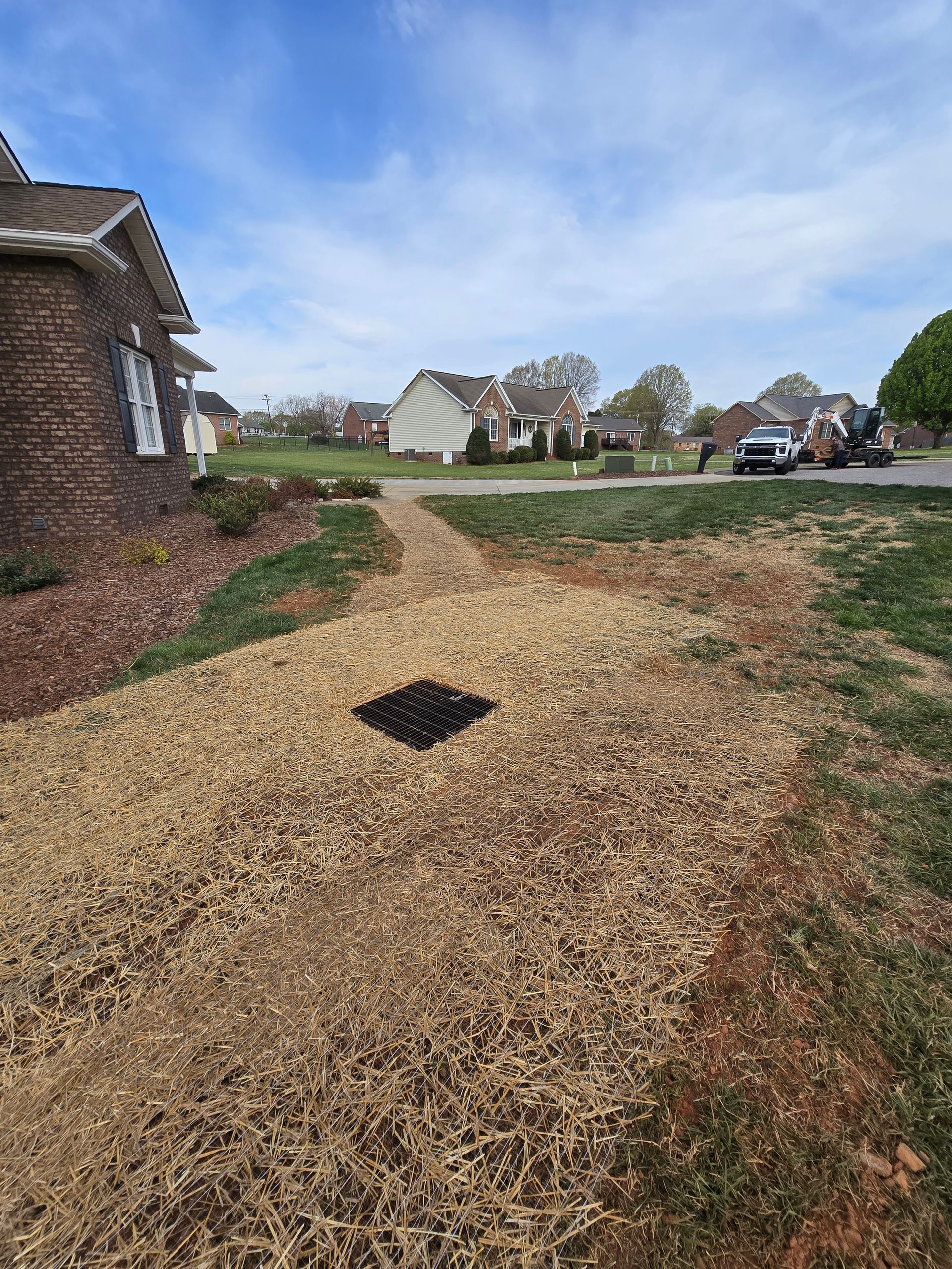 Gravel path beside a brick house, with a landscaped yard and suburban homes under a cloudy sky.