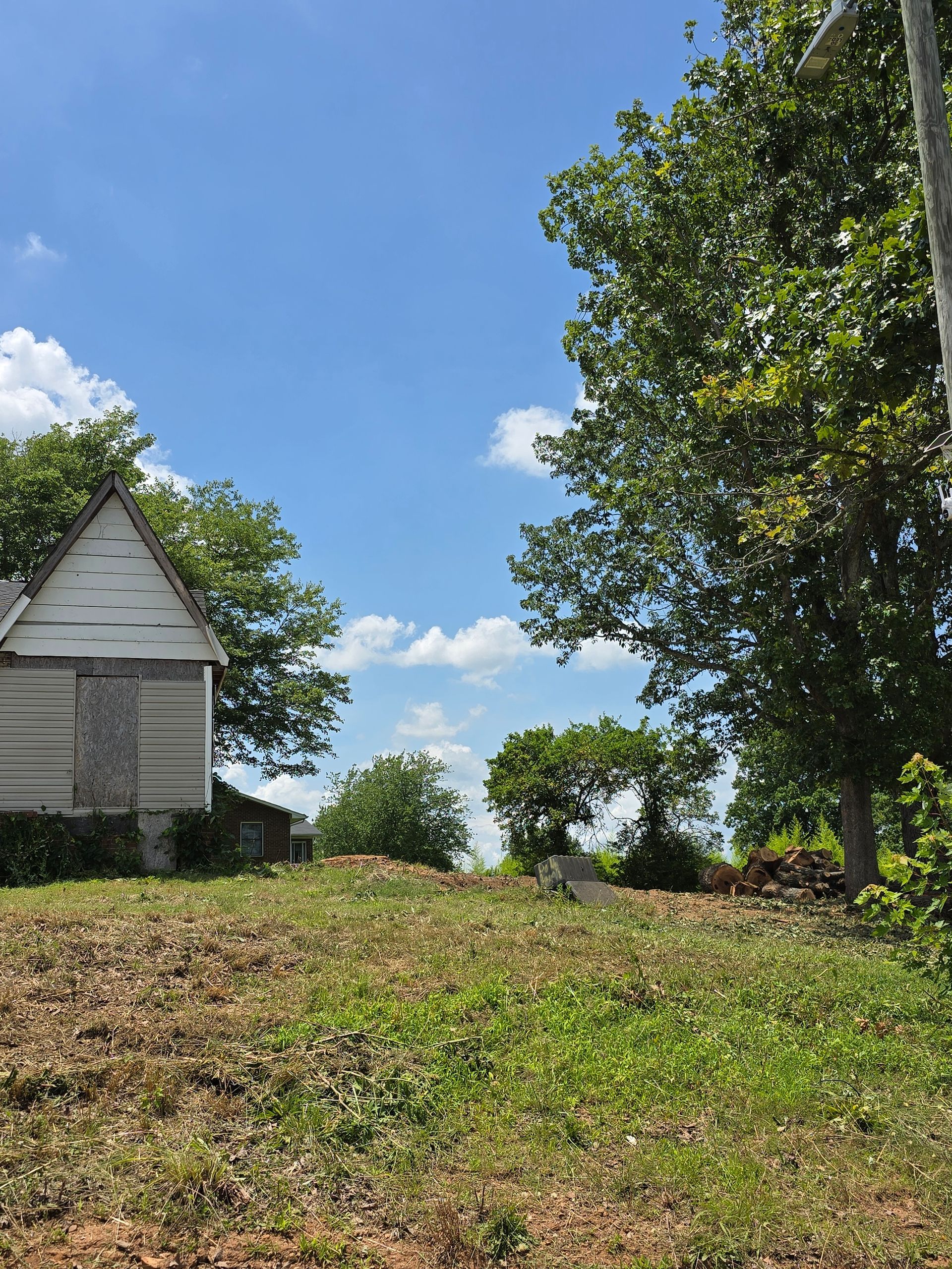 Small white house beside a grassy field with trees under a bright blue sky.