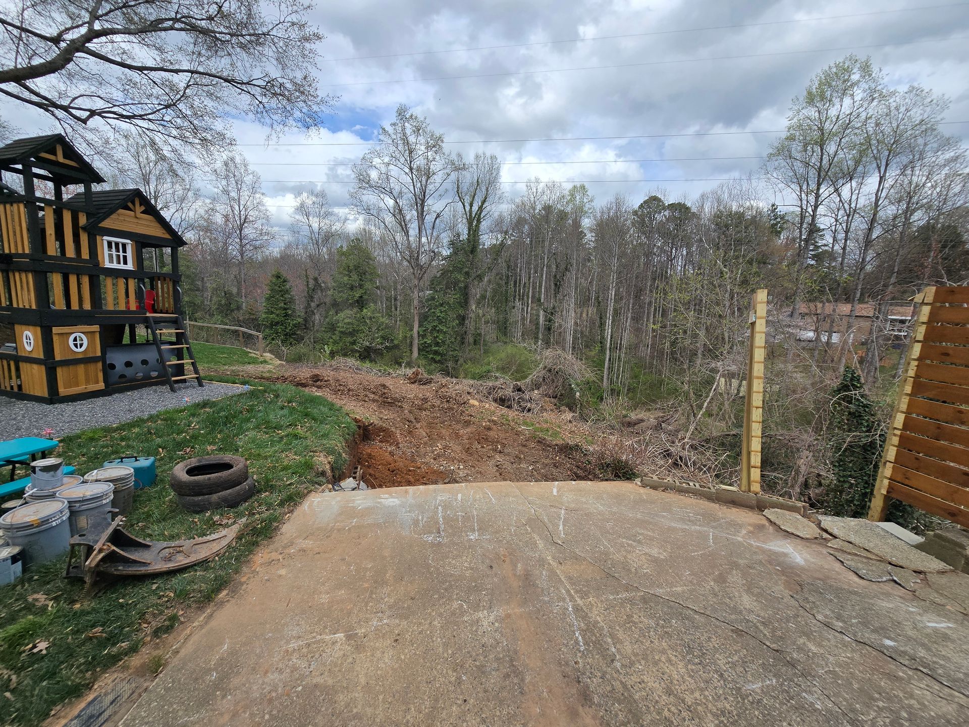 Concrete slab overlooking a wooded yard with a half-timbered house on the left and a wooden fence on the right