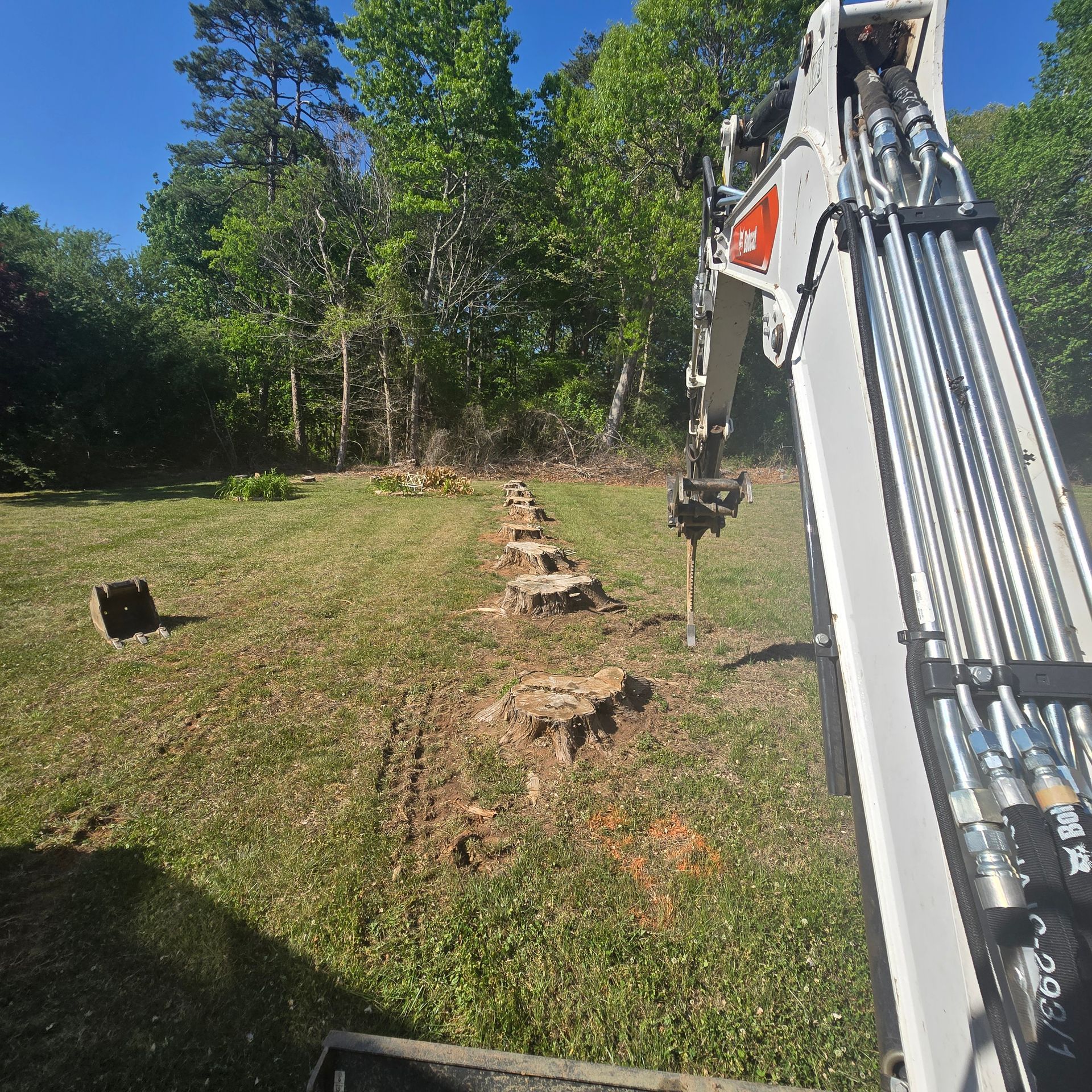 Excavator arm beside a trench line in a grassy yard with trees in the background