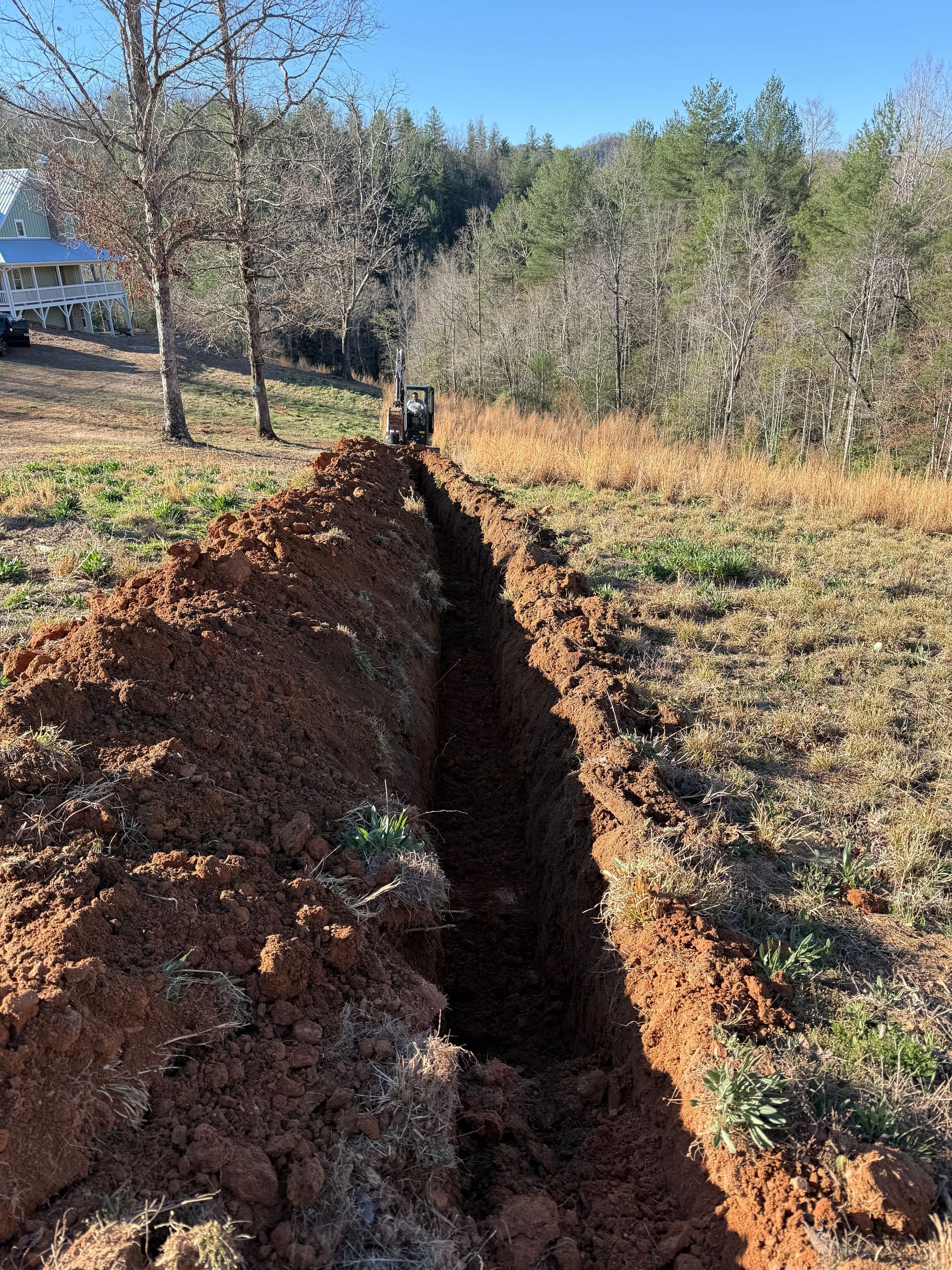 Deep trench cut through a grassy field with trees in the background
