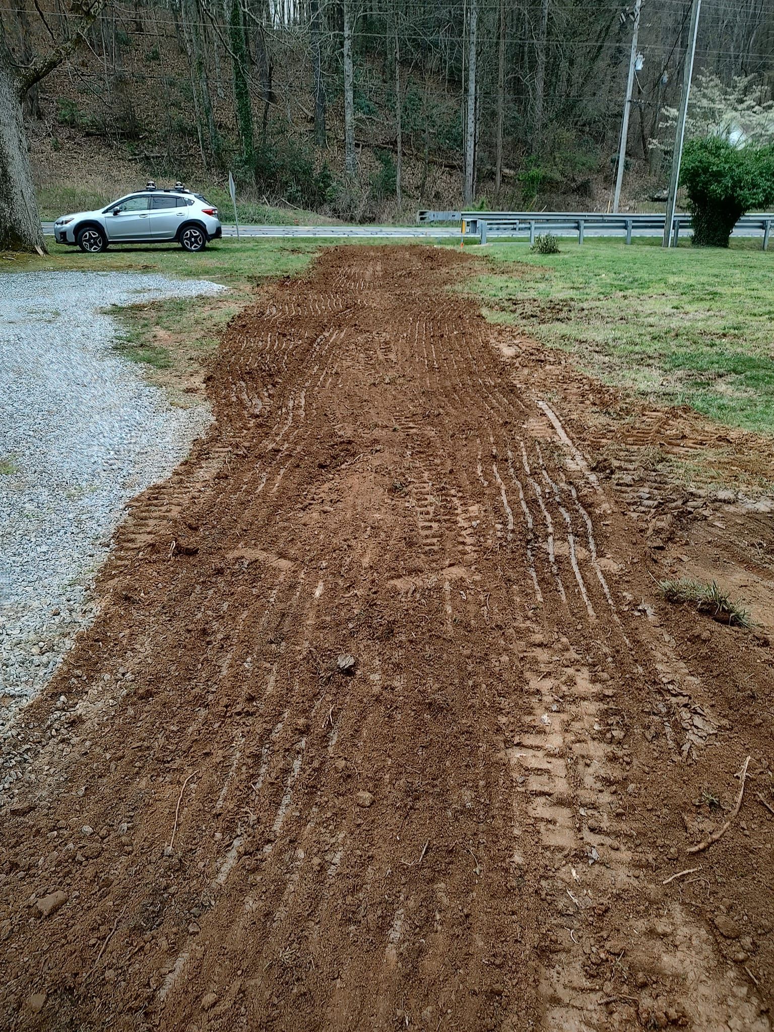 Fresh brown mulch spread along a roadside with a parked silver car and wooded background