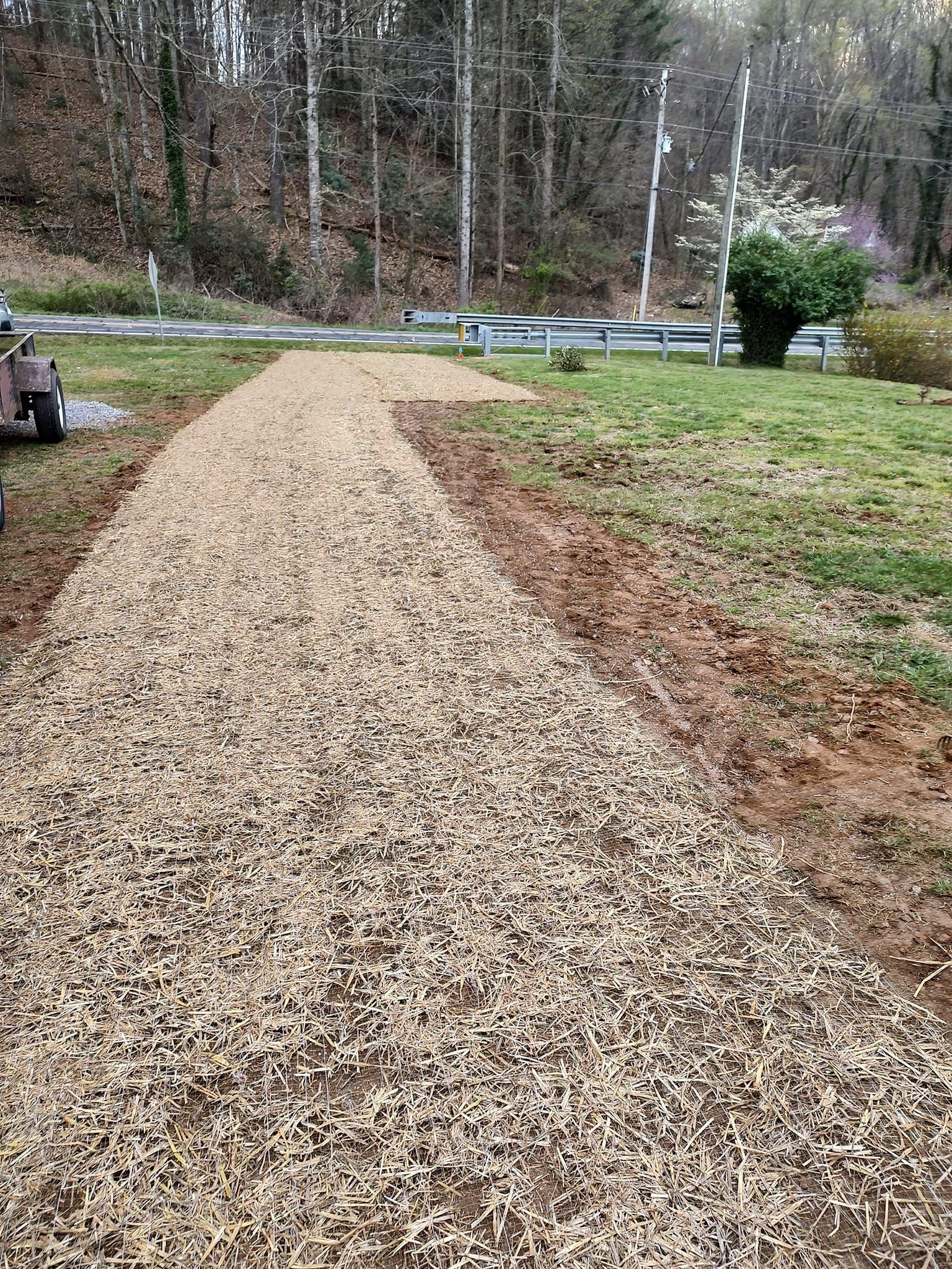 Curved gravel path through a grassy yard toward a road and wooded hillside