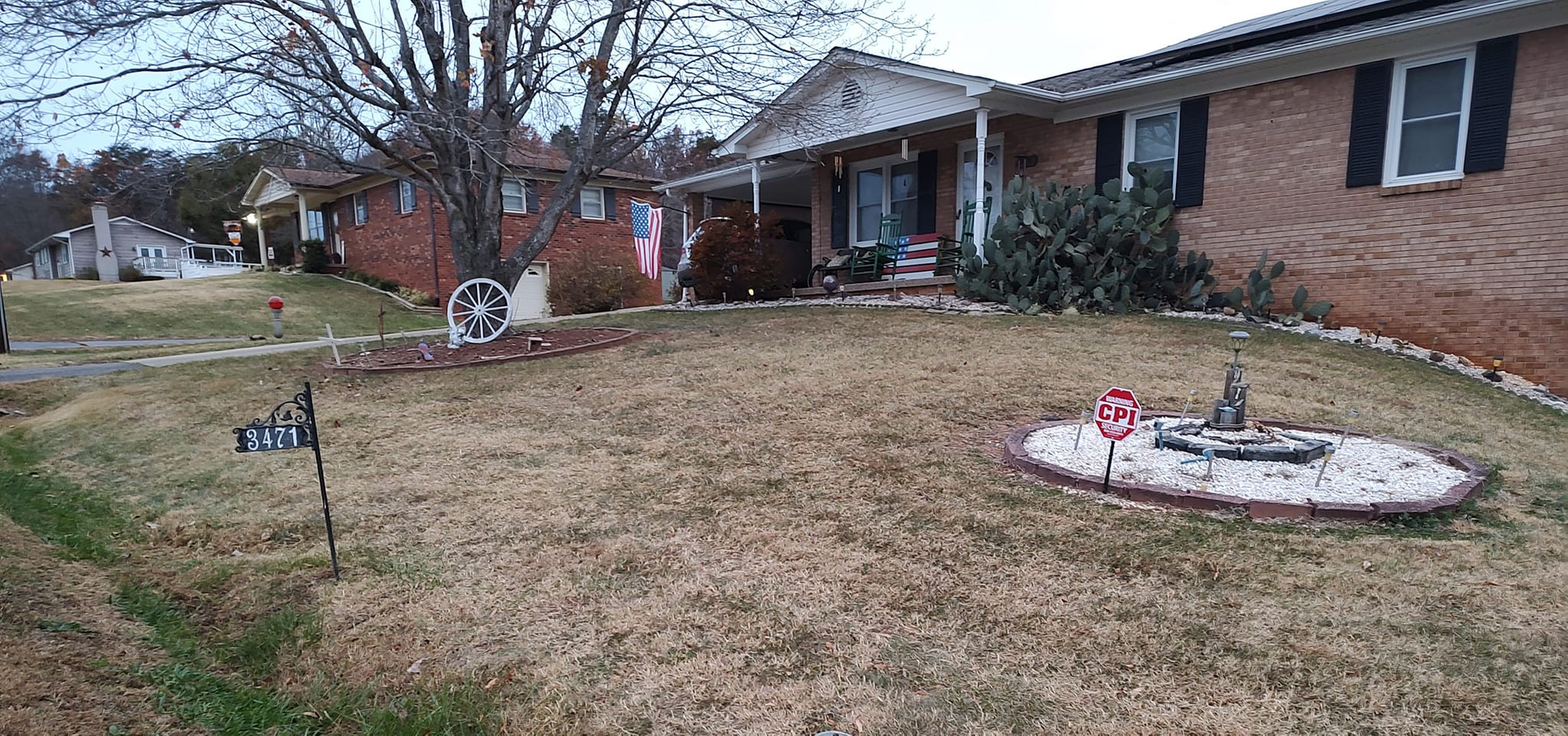Suburban front yard with winter grass, brick house, and a small garden bed near the walkway