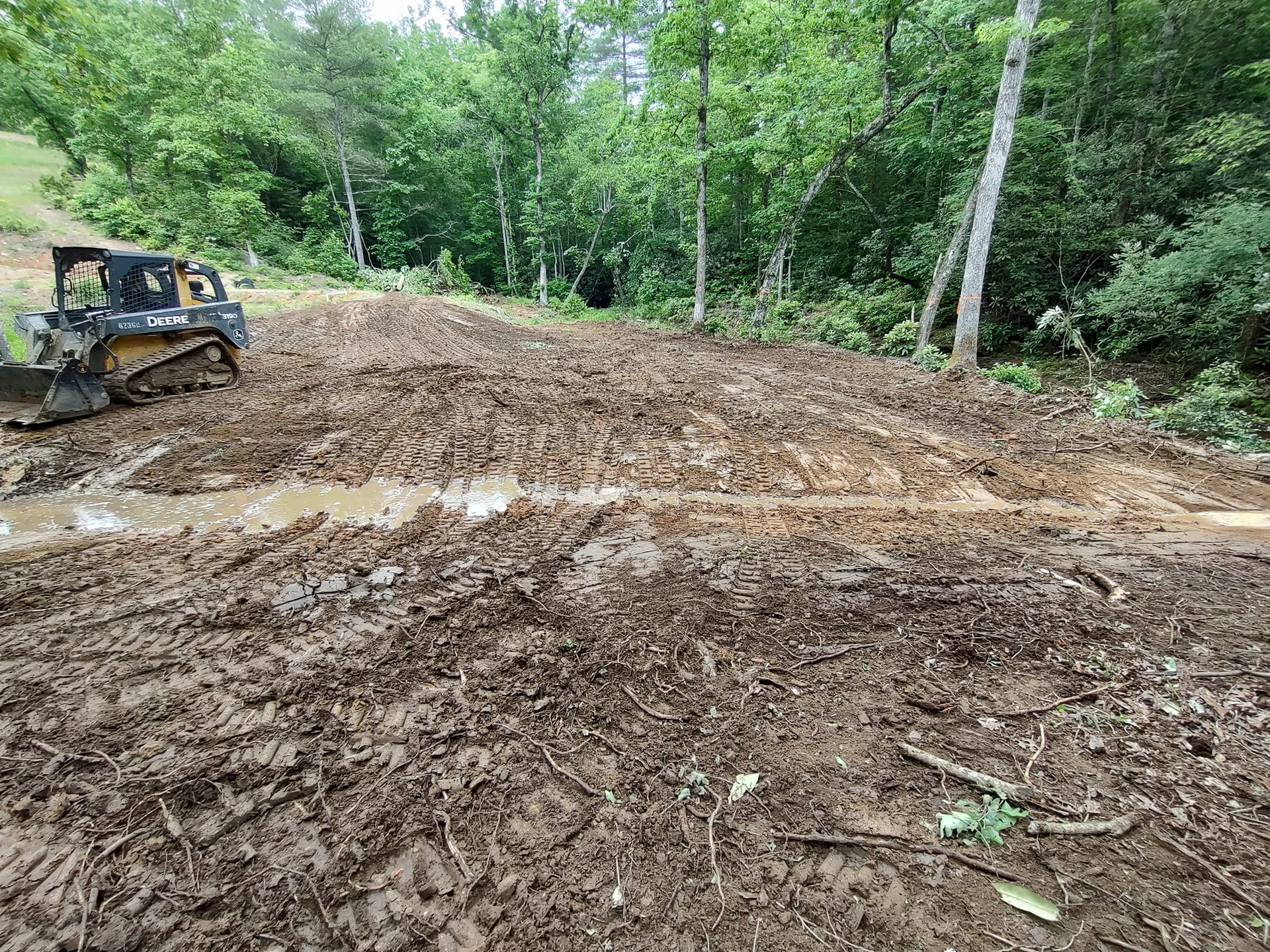 Bulldozer grading muddy dirt clearing in a wooded area