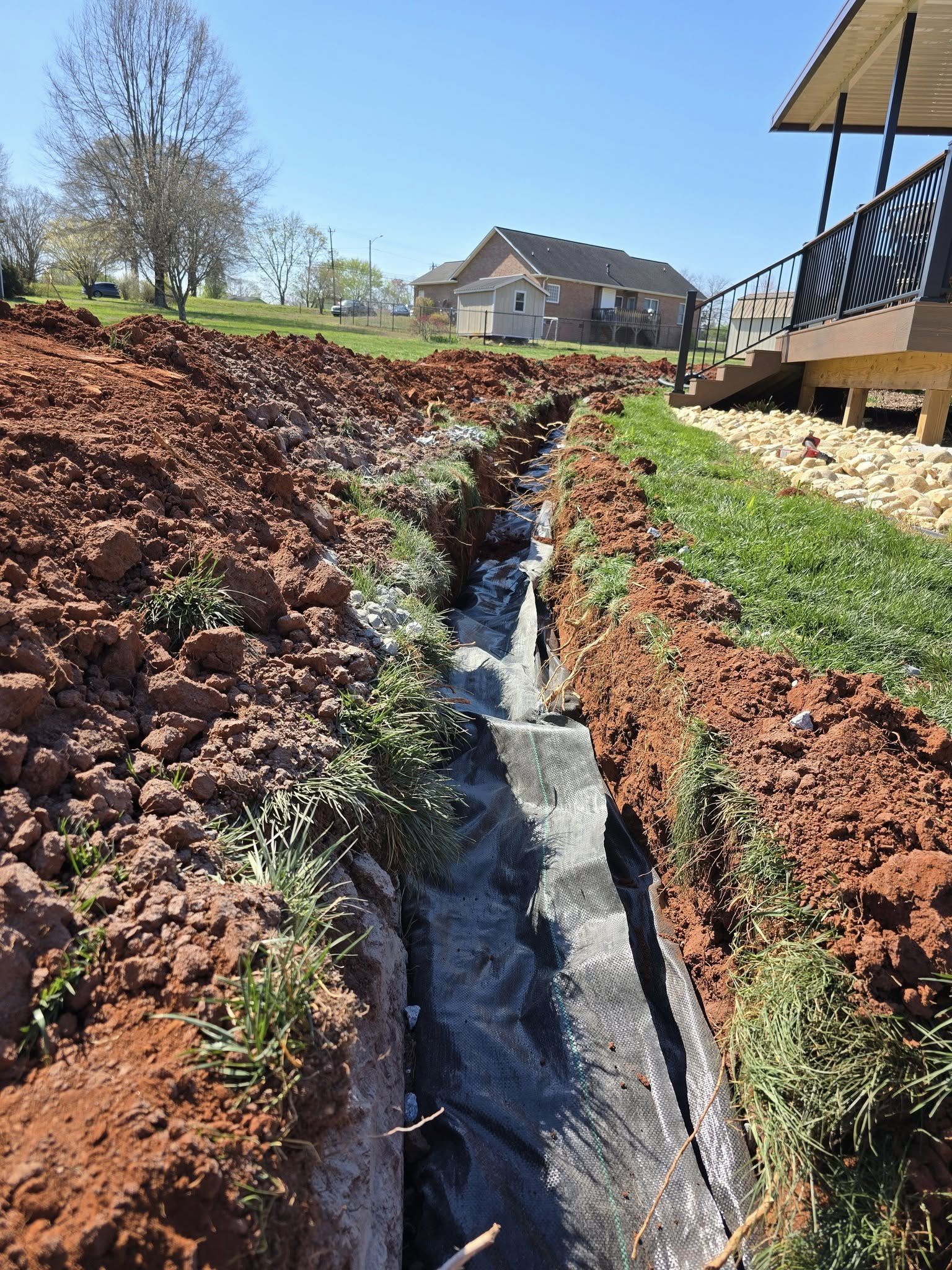 Wooded drainage trench with flowing water between red soil banks near a house and staircase