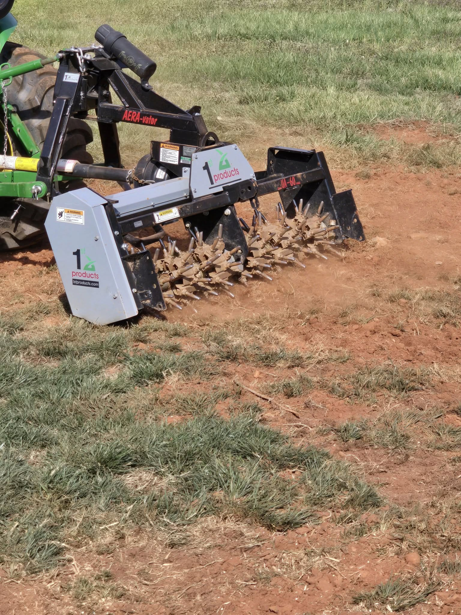 Tractor-mounted tiller churning dry soil in a grassy field