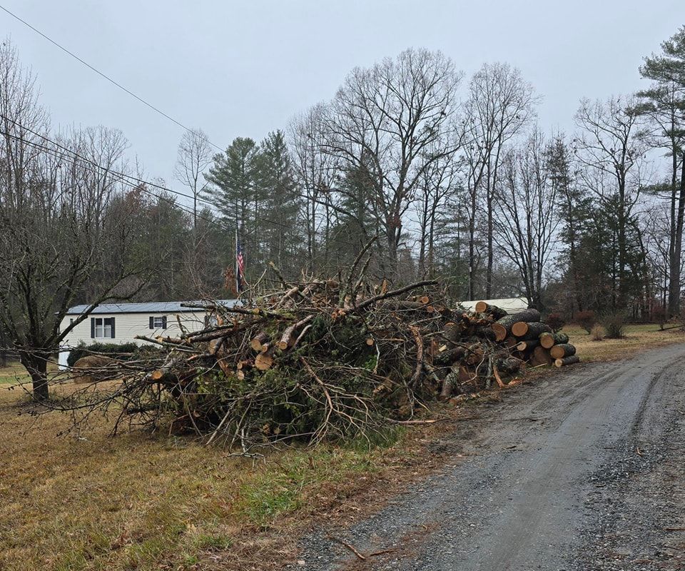 Large pile of cut tree branches beside a gravel road near a house on a cloudy day