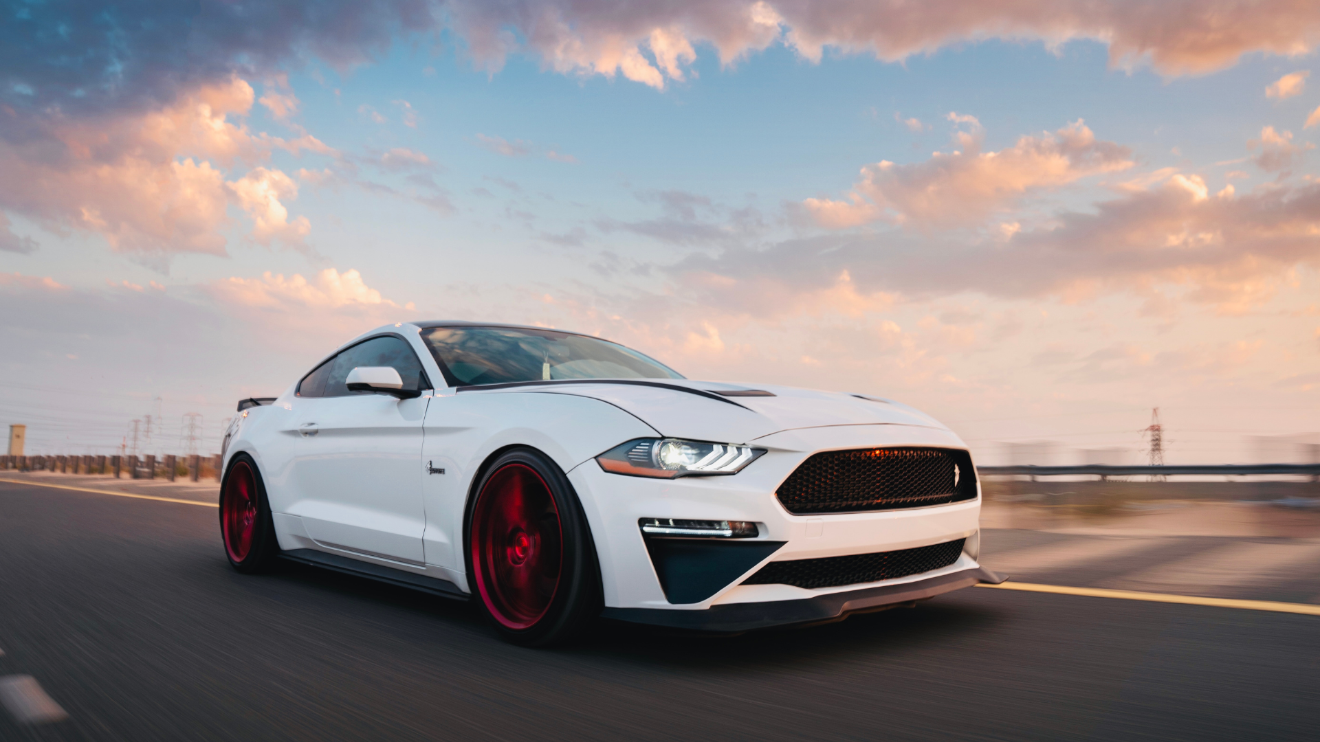 A white ford mustang is driving down a road at sunset.