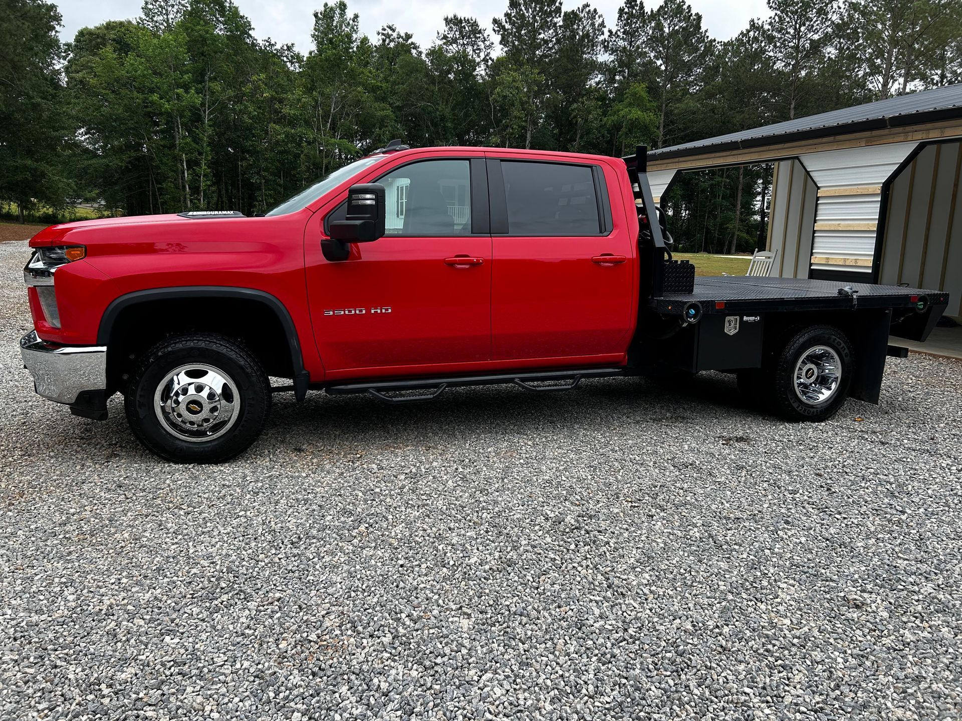 A red truck is parked in a gravel lot next to a trailer.