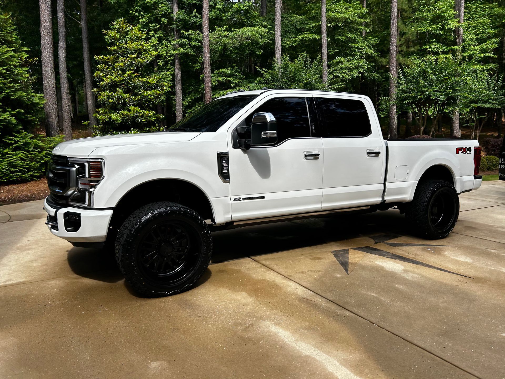 A white pickup truck is parked in a driveway next to trees.