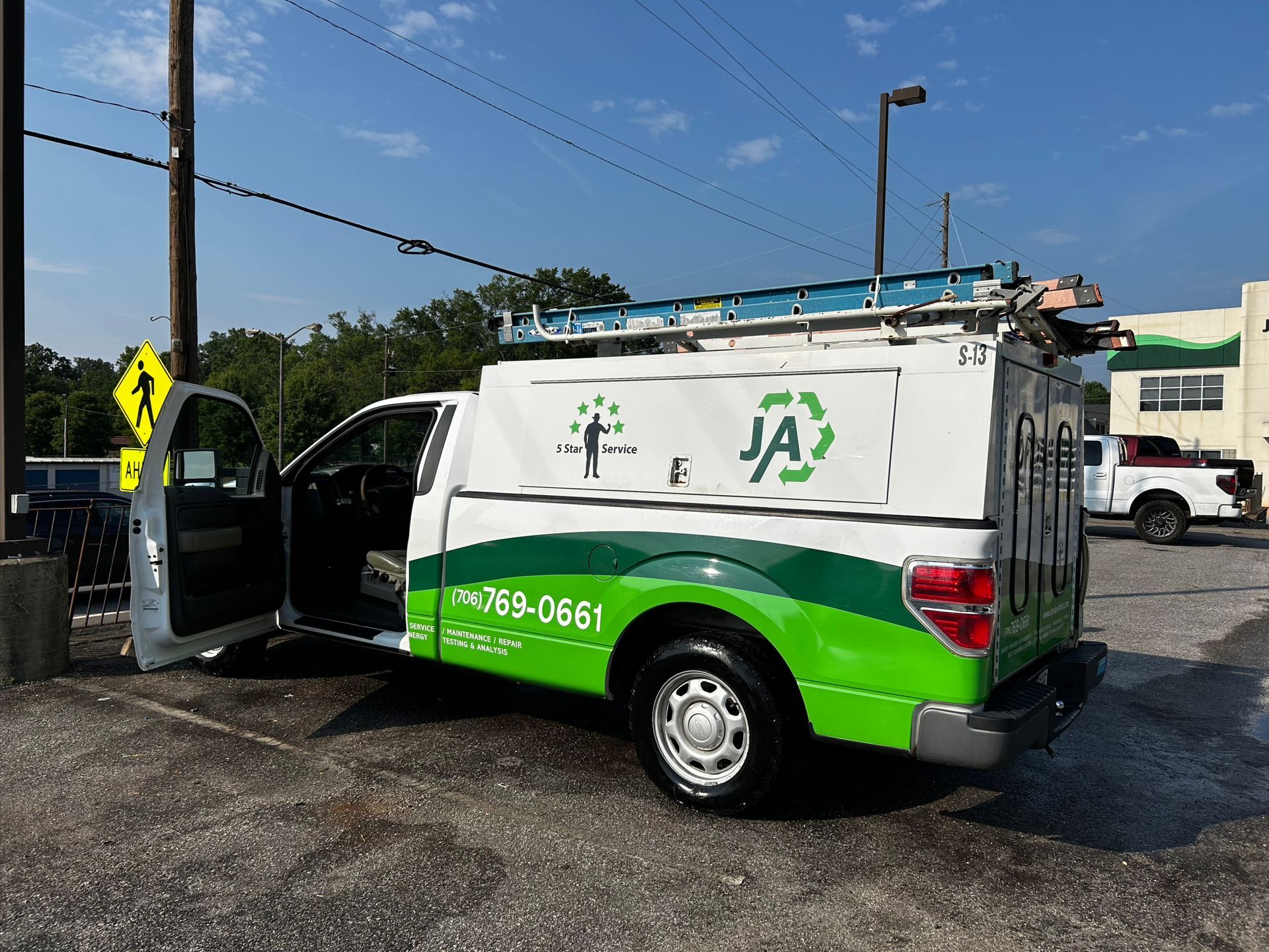 A green and white truck with the door open is parked in a parking lot.