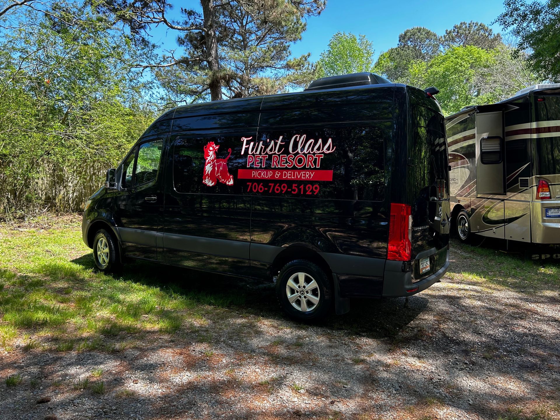 A black van is parked in a grassy area next to a rv.