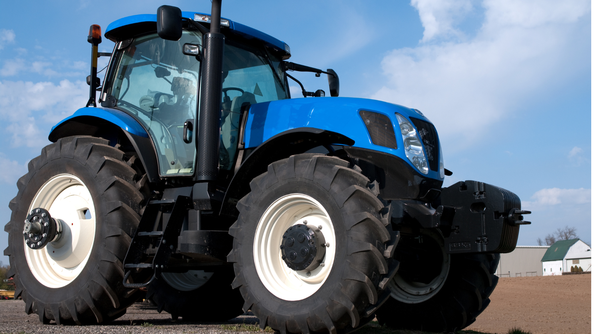 A blue tractor with white tires is parked in a field