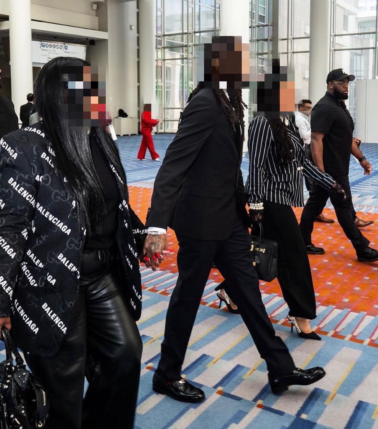 Three people in formal attire walk inside a building with a security guard.