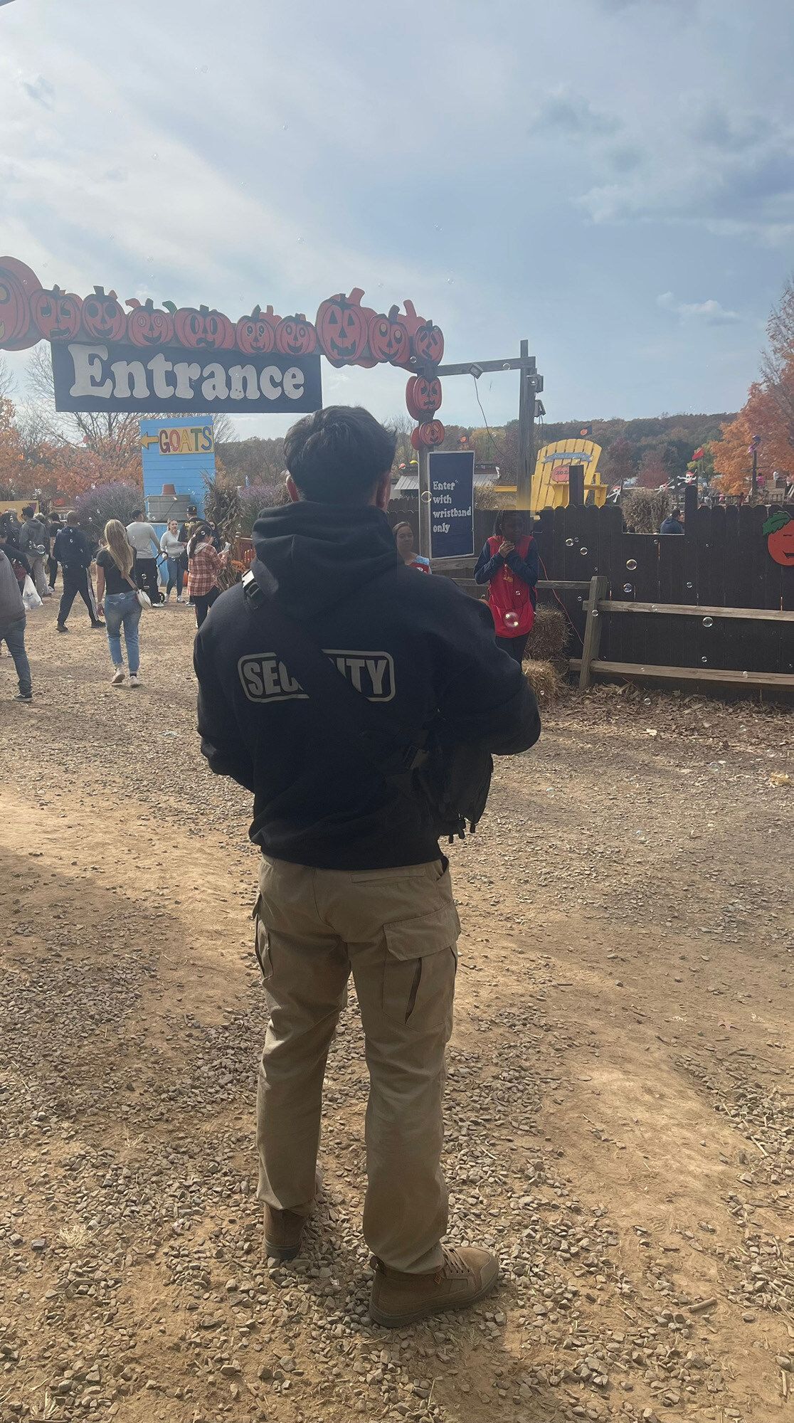 Security guard in black jacket stands at the entrance of an event with a wooden sign that says 