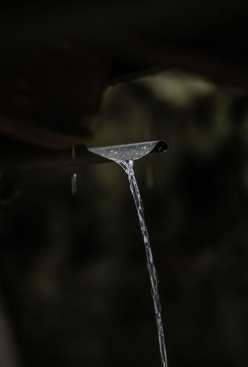 A thin stream of water pours from a small spout into the dark background.
