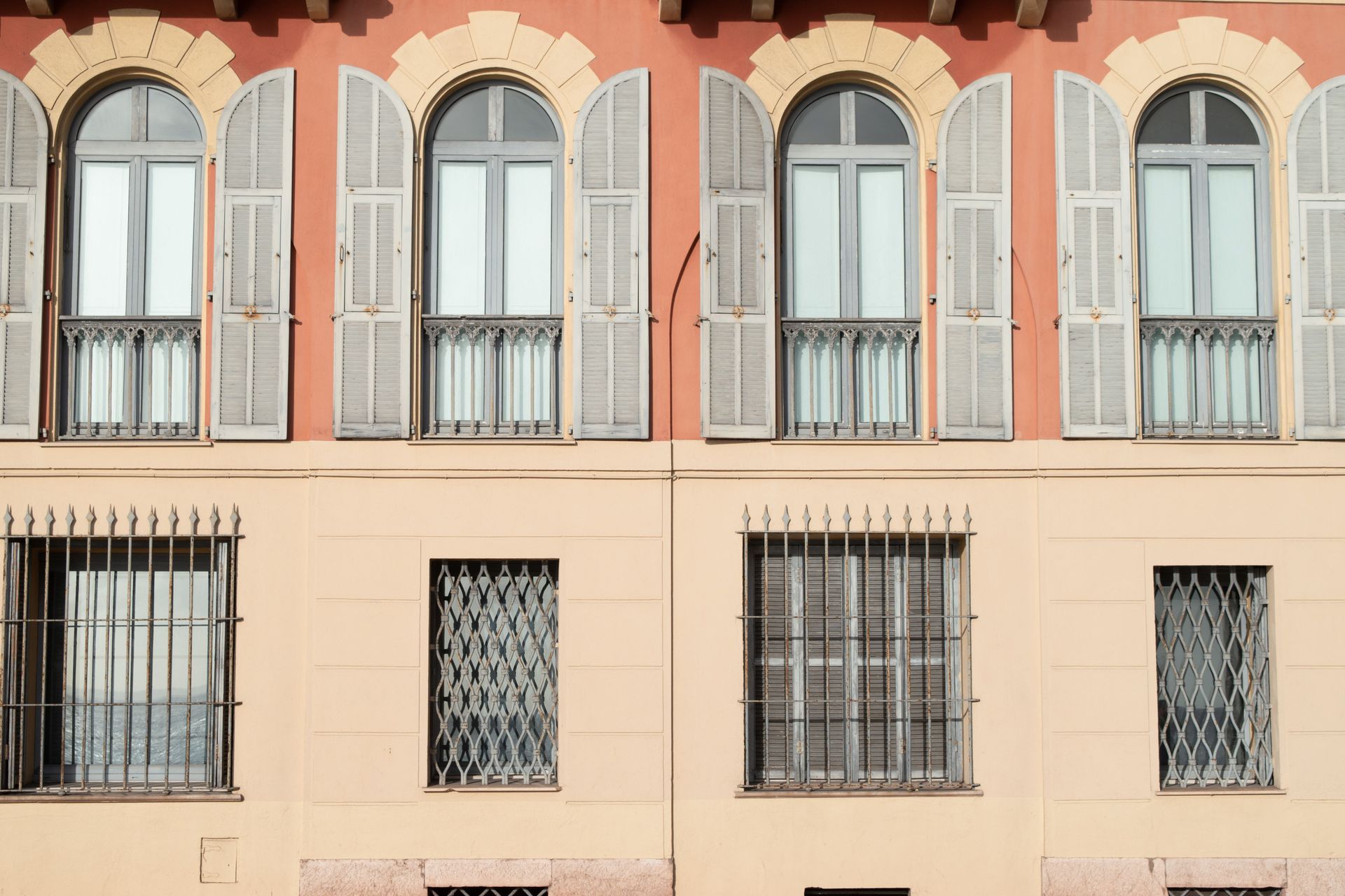 Pastel apartment facade with arched balcony windows and wrought-iron grilles