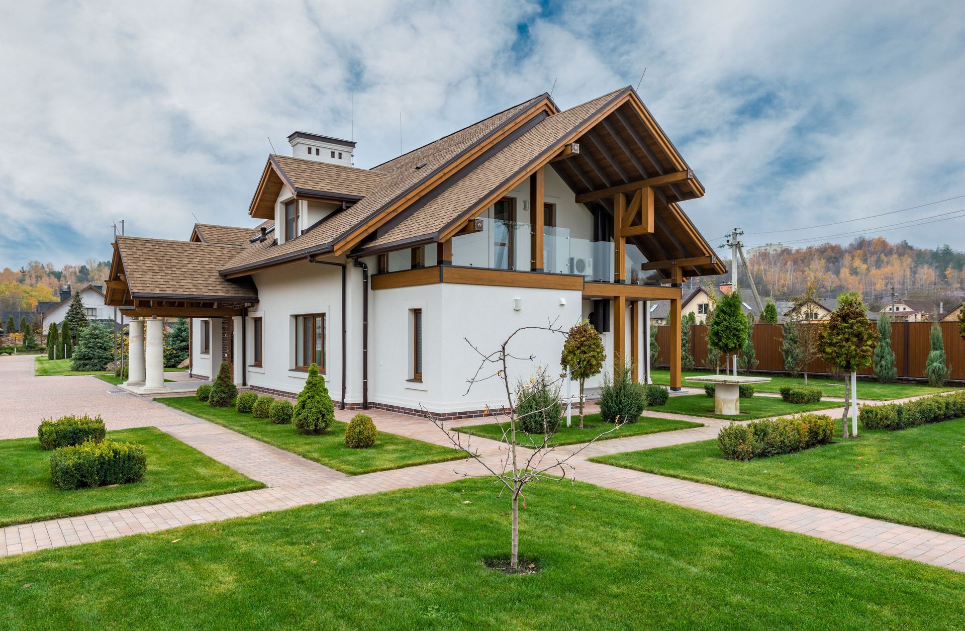 Modern white house with brown roof, manicured lawn, and landscaped garden under a cloudy sky