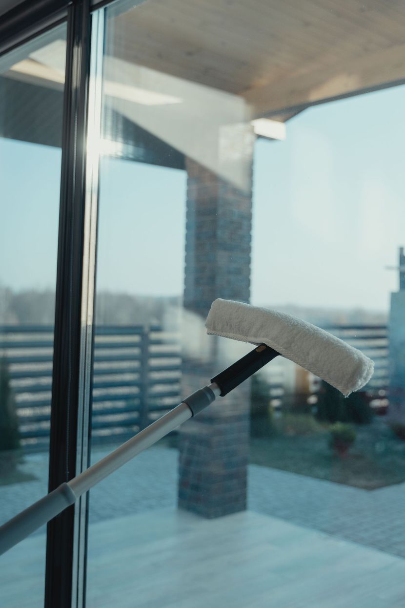 Window cleaner with white pad reaches toward a glass door overlooking a balcony and city view