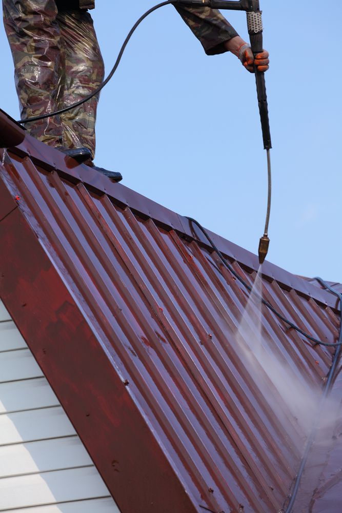 Person Pressure Washing a Brown Metal Roof Against a Blue Sky — Busy Bees Blasting in Trinity Beach, QLD